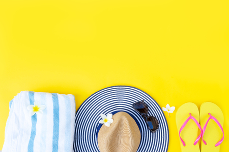 Summer flat lay border with hat, towel and flip-flops on yellow background with copy spaceの写真素材