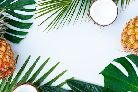 Summer flat lay frame with tropical leaves, coconuts and pineapples frame on gray wooden background...