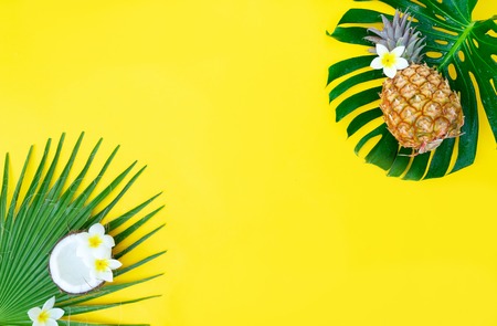 Summer flat lay frame with tropical green leaves, coco and pineapples frame on yellow
