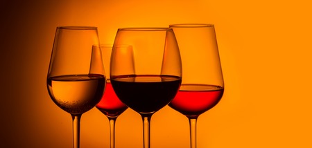 Set of four wine glasses with red, white and rose wine on orange background, banner