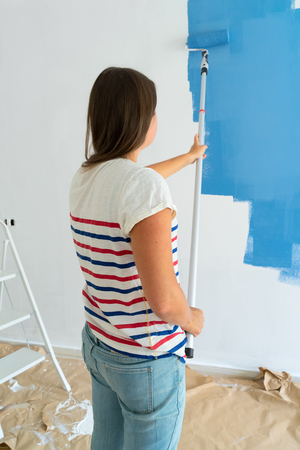 Woman painting wall of her house in blue color, do it yourself home renovation conceptの写真素材