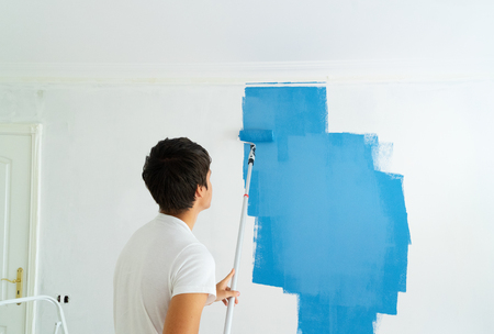 young man painting wall in blue color in the white plastered roomの写真素材