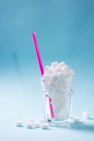 Sugar cubes in glass, diabetes and sugar overuse concept, blue background with copy spaceの写真素材