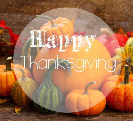 pile of orange and green pumpkins with fall leaves on wooden table with happy Thanksgiving Day greetingsの写真素材