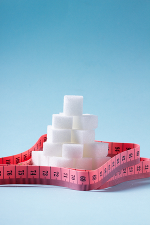 Pile of sugar cubes with pink measuring tape on blue backgroundの写真素材