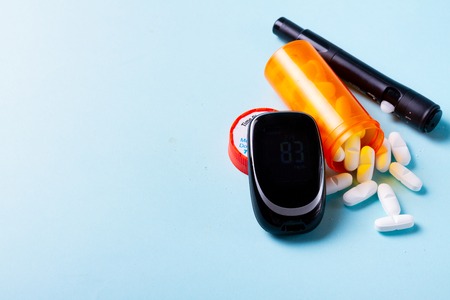 White pills in orange bottle with blood glucose meter on blue background