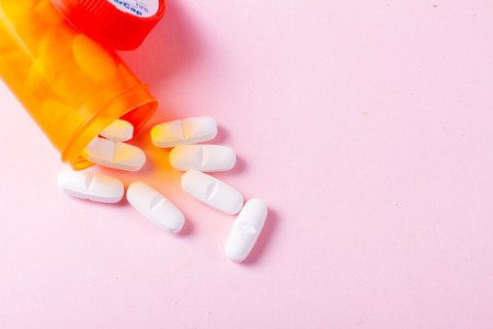 White pills in orange bottle on pink background close up with copy spaceの写真素材