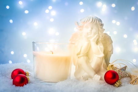 White Christmas  - burning advent candle and cute angel in snow , blue night with lightsの写真素材