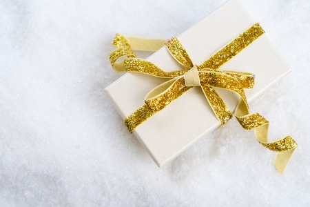 White christmas - gift box with golden ribbon in snow top viewの写真素材