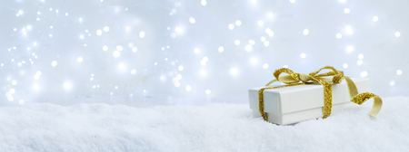 White christmas. gift box with golden ribbon bow in snow bannerの写真素材
