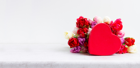 Fresh tulips flowers with heart gift box over white table bannerの写真素材