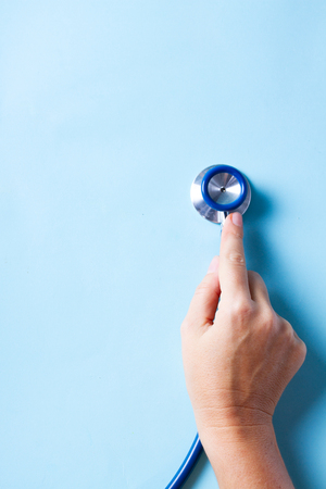 Healthcare concept - someones hand holding stethoscope on blueの写真素材