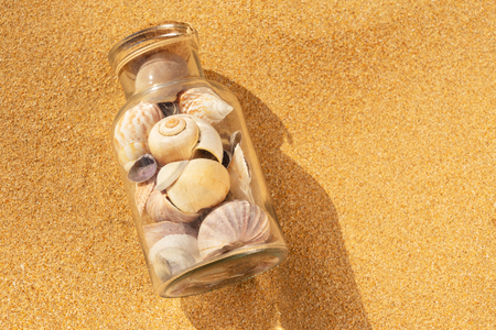 Seashells in glass bottle on summer beach sand, close up top viewの写真素材