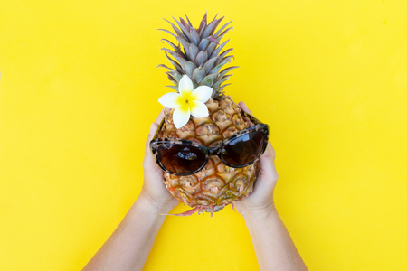 someones hands holding raw pineapple in sunglsses on yellow backgroundの写真素材
