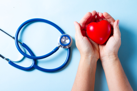 Healthcare concept - two hands holding heart and stethoscope on blueの写真素材