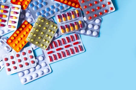 Pile of medical pills and capsules on blue plain background