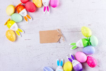 Easter scene with colored eggs and bunnies frame, top view, copy space on empty paper note