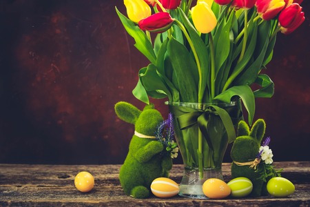 fresh tulip flowers and lesves in vase with easter bunny on dark background, retro tonedの写真素材