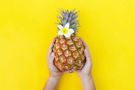 someones two hands holding raw pineapple on yellow backgroundの写真素材