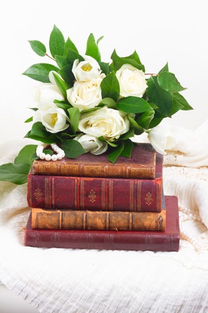 Old book tower with white fresh flowers and green leaves on romantic lace backgroundの写真素材