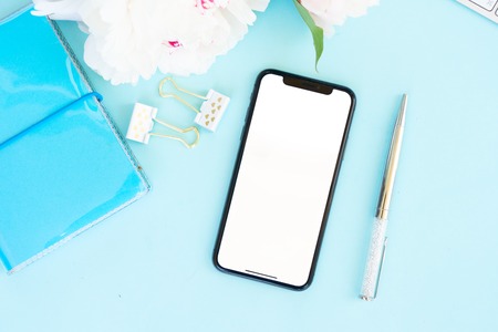 Home office desk with peony flowers and modern phone, top viewの写真素材