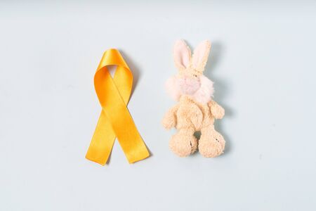 Childrens toy rabbit with a Childhood Cancer Awareness Yellow Ribbon on blue background, top view. Childhood Cancer Day February, 15の写真素材