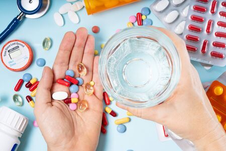 Someones hand holding colorful pills with glass of clear water over blue background, top view. Medical pharmacy concept.の写真素材
