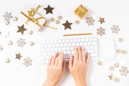 Christmas home office desk with computer keyboard and christmas gold decorations, someones ands typing. Flat lay, top view over white backgroundの写真素材
