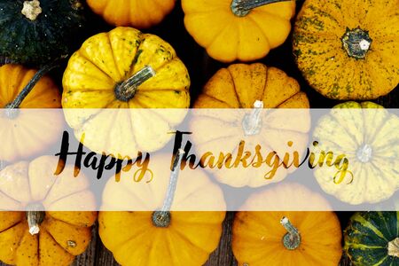 orange and green raw pumpkins on old wooden textured table with happy thanksgiving greetingsの写真素材