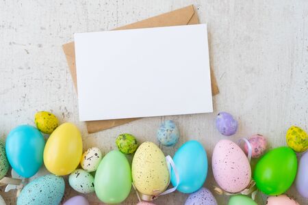 Easter scene with colored eggs border, flat lay on white wooden background, copy space on empty card