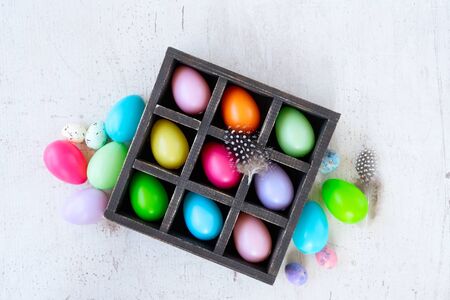 Easter scene with colored eggs in box, flat lay on white wooden backgroundの写真素材