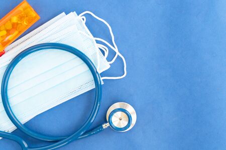 Healthcare concept - stethoscope, masks and pills on blue with copy space, corona viruses concept