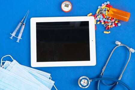 Healthcare and coronavirus concept - stethoscope, masks and pills on blue, copy space on tablet screenの写真素材