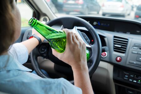 WOman driving and holding a bottle with alchohol. Drunk driving concept
