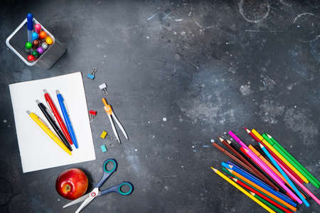Back to school concept with colorful school supplies and apple on blackboard background with copy...