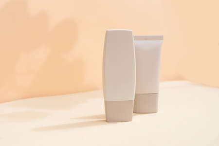 Minimal modern cosmetic products display with two tubes on textured beige background with shadow overlayの写真素材