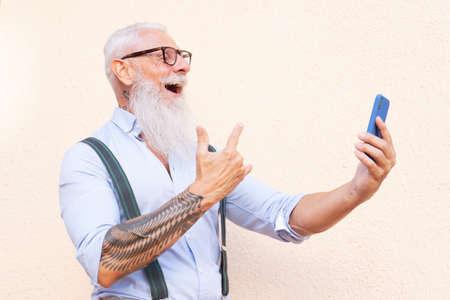 Senior hipster man with tatoo having fun with a phone, happiness, technology and elderly lifestyle people conceptの写真素材