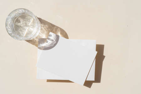 summer stationery mock-up scene. Blank business card and glass of clear water on beige textured table background. Flat lay, top viewの写真素材