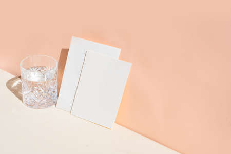 summer stationery mock-up scene. Blank business card and glass of clear water on beige textured...