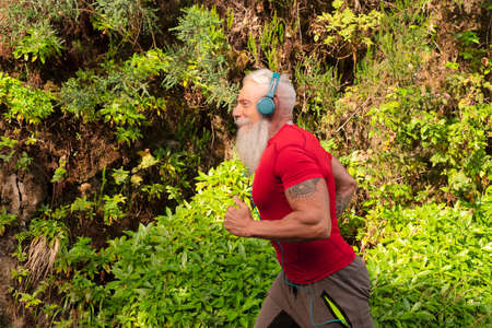 Senior man with white beard doing running outdoor on the nature