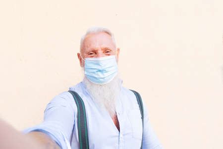 Senior man in mask with modern phone doing selfie during coronavirus outbreak, new normal life...