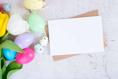 Easter scene with colored eggs and tulips, flat lay on white wooden background with copy space on...