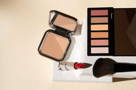 Minimal modern cosmetic scene with make up brushes, eye shadows palette, lipstick, powder, neutral beige colorsの写真素材