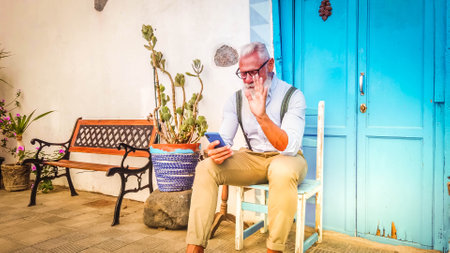 Senior hipster man communicatong online with a phone, new normal, happiness, technology and elderly lifestyle people conceptの写真素材