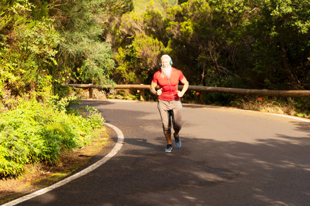 Senior man with white beard doing running outdoor on the nature by the road