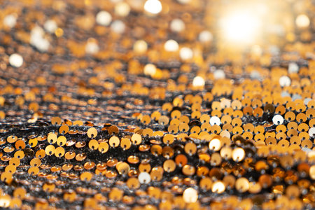 Beautiful Christmas light background. Abstract glitter bokeh and scattered sequins in gold, on black, shallow focusの写真素材
