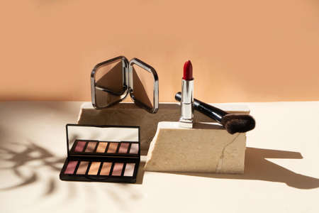 Minimal modern cosmetic scene with make up brushes, eye shadows palette, lipstick, neutral beige backgroundの写真素材