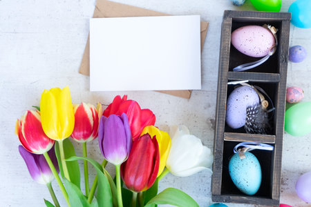 Easter scene with colored eggs and tulips, close up flat lay on white wooden background with copy...