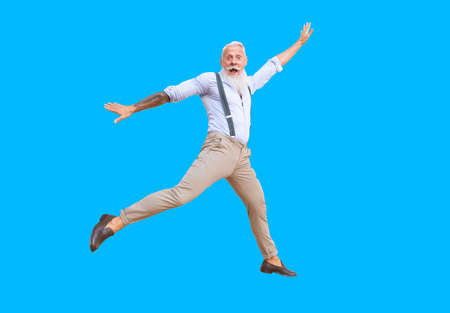 Senior hipster man with tatoo having fun jumping on blue background, happy senior people lifestyleの写真素材