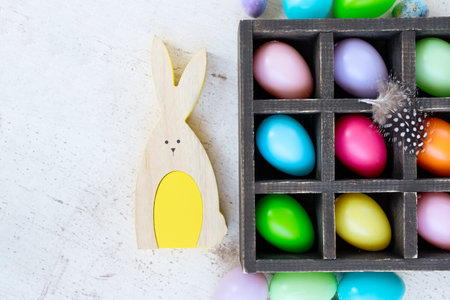 Easter scene with colored eggs and rabbit, flat lay on white wooden background